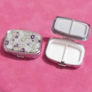 Purple flowers next to the greenery. Pill Case